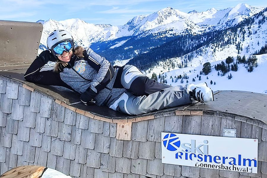Eine Schifahrerin liegt auf einer Liege und lächelt in die Kamera