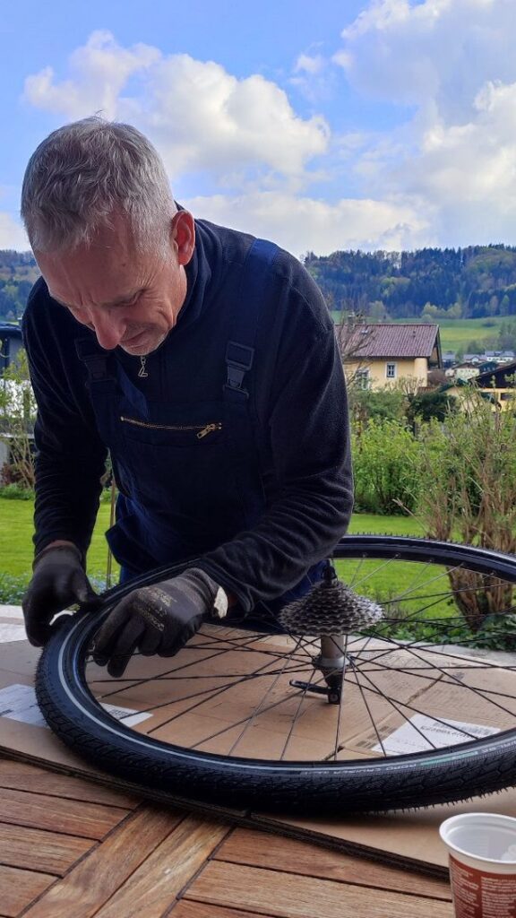 Ein Mann steht an einem Arbeitstisch auf einer Terrasse und repariert einen Fahrradreifen 