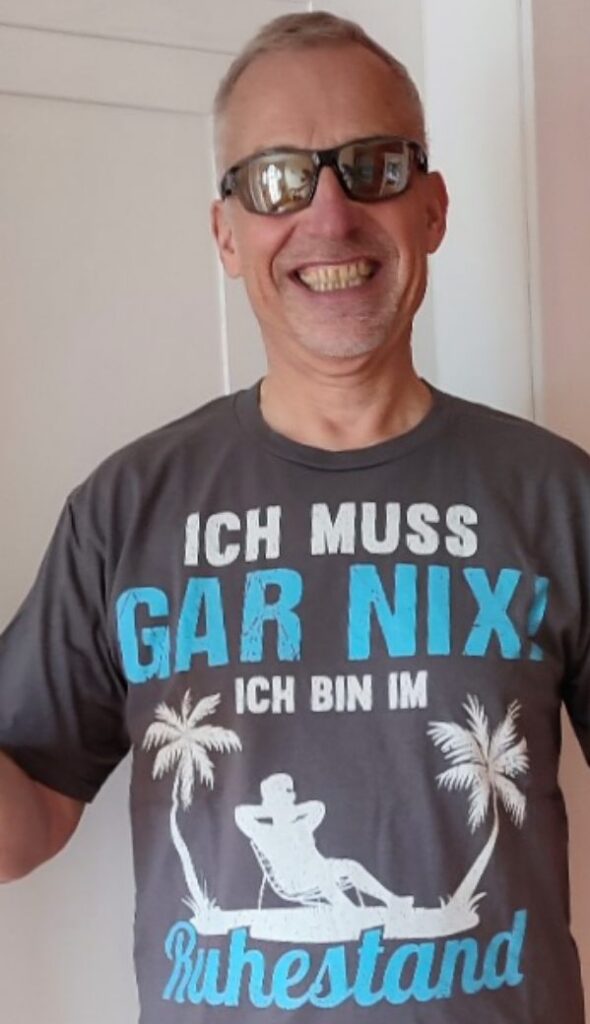 Ein Mann mit Sport-Sonnenbrille und einem T-Shirt mit Textaufdruck "Ich muss gar nix - ich bin im Ruhestand"