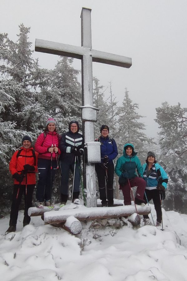 eine Wandergruppe mit 6 Personen im Schnee neben einem Gipfelkreuz