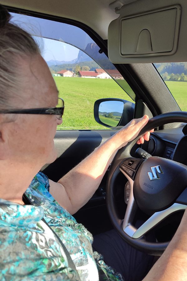 eine Frau mit Brille lenkt ein Auto der Marke Suzuki - sie hält das Lenkrad mit beiden Händen und richtet ihren Blick nach vorne durch die Windschutzscheibe